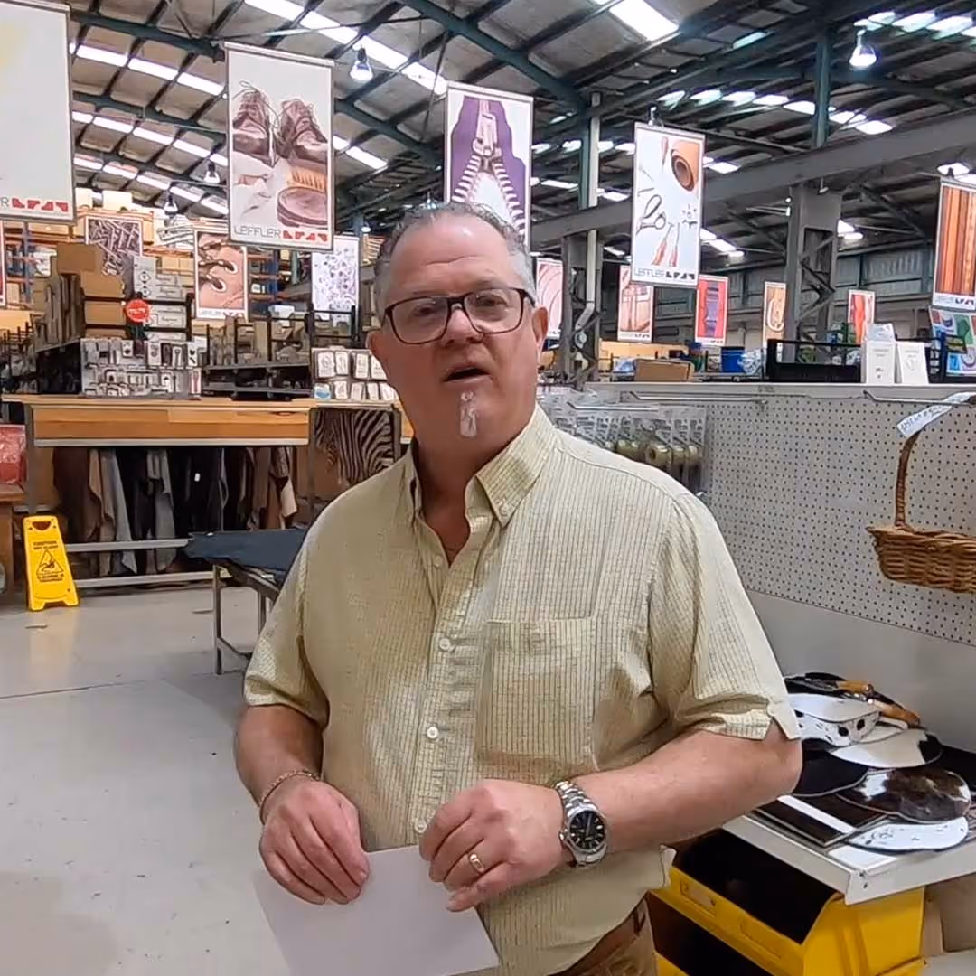 Man wearing glasses and a yellow short-sleeve shirt standing inside a hardware or craft store holding a white sheet of paper.